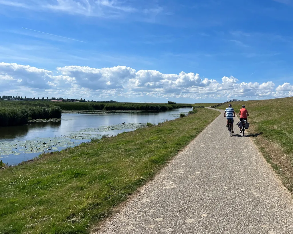 Twee fietsers op een fietspad langs een kanaal op een zonnige dag